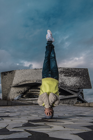 Un danseur de Hip-Hop, les mains sur le visage, le corps à la verticale, tête sur le sol, pieds en l'air