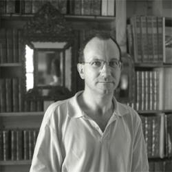 Portrait photographique de Xavier Bzato en noir et blanc, debout devant une bibliothèque.