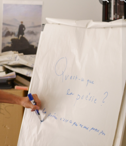 Photo d'une main écrivant sur un tableau, Qu'est-ce que la Poésie ?